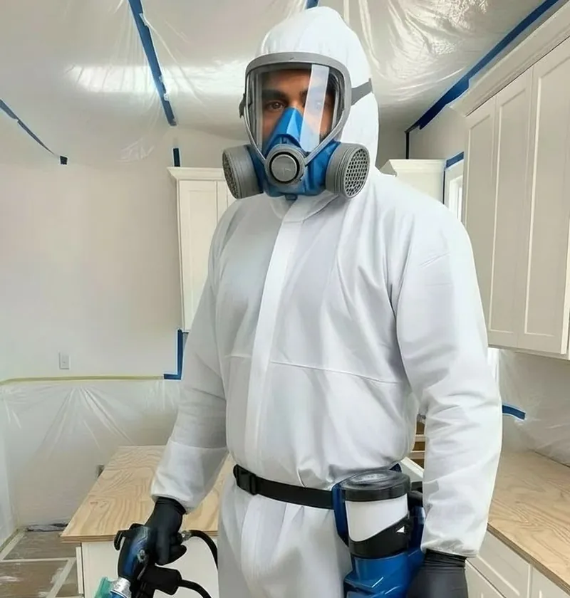 Silvio in a spray suit and respirator, in a kitchen masked off with plastic before spraying