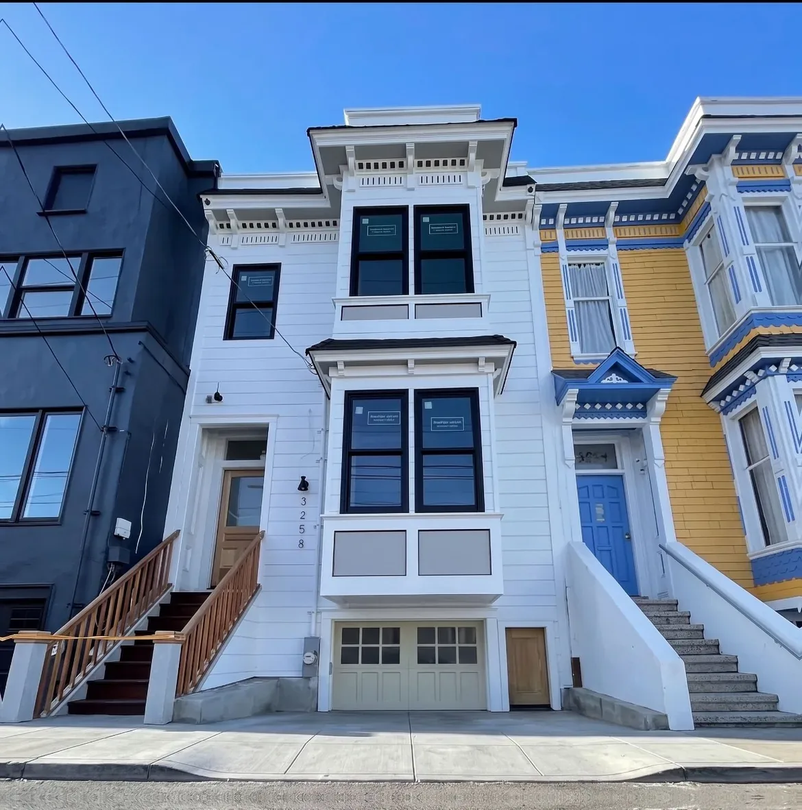 White Victorian row house with dark trim after repainting, between a dark grey and a yellow neighbour