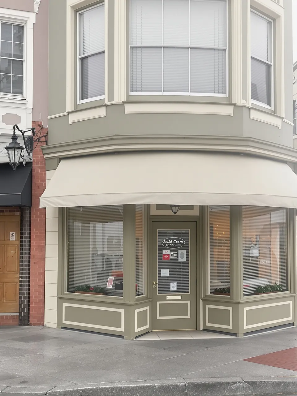 Corner storefront painted olive green with a cream awning