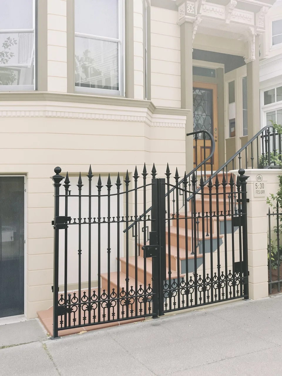 Matte black wrought-iron gate and stair railing in front of a cream Victorian